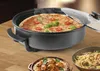 A pizza is being cooked in an electric pan, with other dishes of pasta and meatballs visible in the foreground. Anteprima dell’immagine prodotto