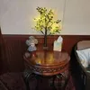 A decorative tree with lights sits on a round wooden table next to a cross and a tissue box. Produktbild-Vorschau