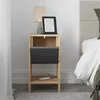 A bedside table next to a bed, with a lamp and e-reader on top, and a phone charging on the shelf.