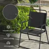 A black folding garden chair is shown outdoors on a sandy surface, with lush green foliage and palm trees in the background. A close-up inset highlights the fabric material. Náhľad obrázku produktu