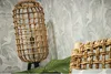 A close-up of a rattan floor lamp and a woven basket against a tropical leaf patterned wallpaper. Produktbild-Vorschau