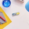 A pack of gum is placed on a white surface next to a notebook and pen, with a glass of iced drink in the background. Produktbild-Vorschau