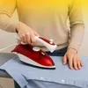 A person is ironing a blue shirt with a red and white steam iron. Produktbild-Vorschau