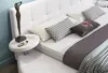A white upholstered bed with pillows and a bedside table. Produktbild-Vorschau