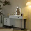 A white vanity table with a mirror and drawers, next to a plant and a floor lamp. Náhľad obrázku produktu