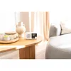 A white portable radio sits on a wooden coffee table next to a vase and candles, with a couch in the background. Náhled obrázku produktu