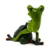 A ceramic frog figurine sitting on a green sack, viewed from the back. Produktbild-Vorschau