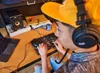 A person wearing headphones and a yellow cap is using a DJ controller in a room with a laptop and a speaker. Produktbild-Vorschau