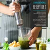A person is using an immersion blender to make pesto in a tall glass container, with ingredients like basil, parmesan, and olive oil visible. Náhľad obrázku produktu