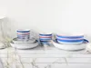 A set of striped ceramic dishes and mugs arranged on a wooden surface against a white background. Náhľad obrázku produktu