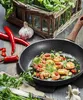 A frying pan with cooked shrimp and chili peppers, surrounded by fresh ingredients like garlic and parsley, on a wooden table. Voir les images du produit