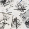 A collection of sketches and art supplies, including pencils and a sharpener, arranged on a white surface. Produktbild-Vorschau