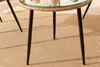 A close-up view of the legs and underside of a round bistro table with a woven rattan edge and a glass top, placed on a striped rug. Produktbild-Vorschau