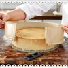 A person is using a cake ring to adjust the size of a cake on a wooden cutting board. Produktbild-Vorschau