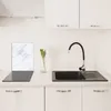 A clean, modern kitchen counter with a sink, faucet, and a glass cutting board with a marble pattern. Produktbild-Vorschau