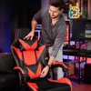 A man is adjusting a gaming chair in a room with a computer setup. Náhled obrázku produktu