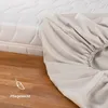 A close-up of a fitted sheet being placed on a mattress, with a wooden floor in the foreground. Produktbild-Vorschau
