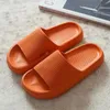 Paar leuchtend orangefarbene Slide-Sandalen mit dicker Sohle und strukturiertem Fußbett auf hellgrauem Teppich Náhľad obrázku produktu