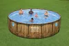 A round above-ground swimming pool with a wood-look exterior, filled with water and with five people swimming in it, set on a green lawn. Produktbild-Vorschau