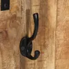 A close-up shot of a black metal coat hook mounted on a wooden surface. Produktbild-Vorschau