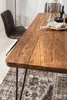 A close-up view of a wooden dining table with metal legs, set in a dining room with a chair and a rug. Produktbild-Vorschau