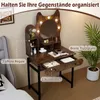 A vanity table with a mirror and lights, set up in a room with a bed and a plant. Podgląd zdjęcia produktu