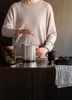 A person is using a French press on a dark wooden countertop, with a jar of herbs and a mug nearby. Náhled obrázku produktu