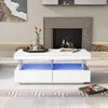 A modern white coffee table with LED lights and two drawers is placed in a living room setting with a fireplace in the background. Voir les images du produit