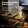 A person wearing headphones is relaxing on a couch, with a lamp in the shape of a bottle on a table in the background. Anteprima dell’immagine prodotto