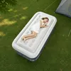 A woman is sleeping on an inflatable mattress outdoors on the grass, with a tent in the background. Produktbild-Vorschau