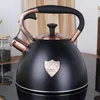 A black kettle with copper accents is shown on a black surface, with jars of herbs in the background. Náhled obrázku produktu