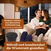A couple is sitting on a couch in front of a fireplace, enjoying a warm drink. Produktbild-Vorschau