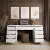 A modern white desk with multiple drawers, a laptop, a lamp, and artwork on the wall. Produktbild-Vorschau