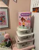 A magnetic book is placed on top of a stack of decorative boxes, with a framed picture and a small decorative plant to the left. Produktbild-Vorschau