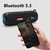 A hand holding a smartphone displaying a music app, with a portable Bluetooth speaker in the background. Produktbild-Vorschau