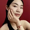 A close-up shot of a woman's face and hand, wearing a bracelet. Produktbild-Vorschau