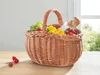 A wicker basket filled with fresh produce and a baguette sits on a wooden table. Produktbild-Vorschau