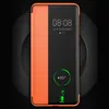 A smartphone with a flip case is shown on a black circular stand, with the phone screen displaying the time and charging status. Produktbild-Vorschau