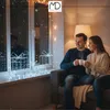 A couple sits on a couch by a window, holding mugs of hot drinks and looking out at falling snow. Decorative illuminated gift boxes are on the windowsill. Podgląd zdjęcia produktu