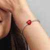 A close-up shot of a person's arm wearing a silver bracelet with a red heart-shaped charm. Produktbild-Vorschau