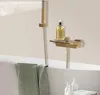 A luxurious gold shower faucet set with a hand shower and a shelf holding a bottle of soap, mounted on a wall above a bathtub with a green towel draped over the edge. Podgląd zdjęcia produktu