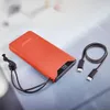 An orange power bank with cables on a light gray surface. Voir les images du produit