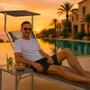 A man relaxing on a lounge chair by a pool at sunset. Produktbild-Vorschau