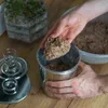 A person is shown placing a portion of ground meat into a stainless steel cooking pot. Produktbild-Vorschau