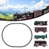A toy train set with multiple cars and tracks, set against a backdrop of mountains and rolling hills. Produktbild-Vorschau