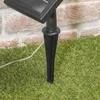 A close-up view of a solar-powered light stake inserted into the grass, with a brick wall in the background. Produktbild-Vorschau