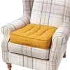 A yellow seat cushion is placed on a plaid armchair. Náhled obrázku produktu
