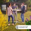 People are gathered around a high table in an outdoor setting, with a tent in the background. Produktbild-Vorschau