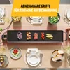 A top-down view of a table set for a meal, featuring a grill plate with food and various side dishes. Voir les images du produit
