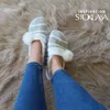 A person's legs wearing jeans and fuzzy slippers, standing on a fluffy rug. Podgląd zdjęcia produktu